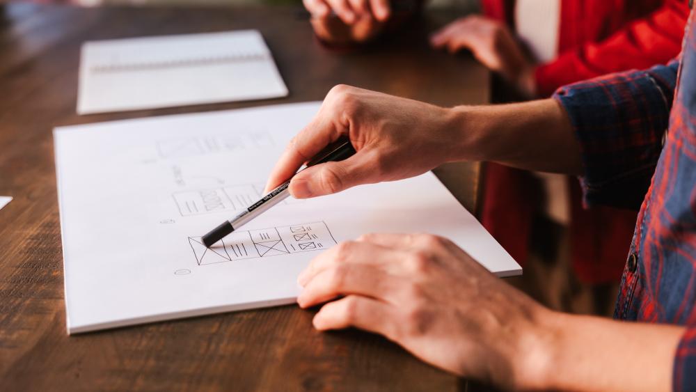 Wireframes drawn on paper with hands pointing at an element (decorative) 
