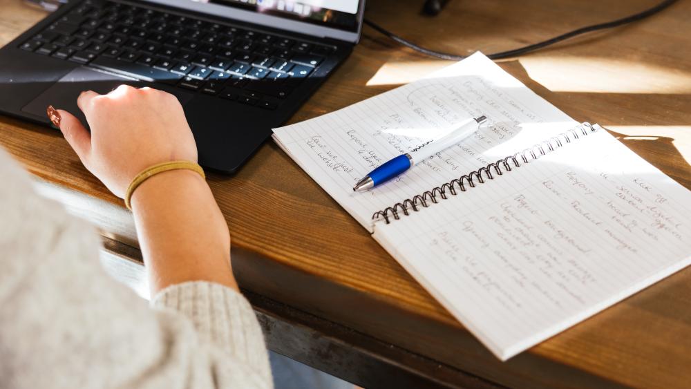 Person making notes with an open laptop