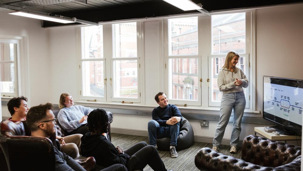 five people watching someone present a process flow chart in an office with big windows 