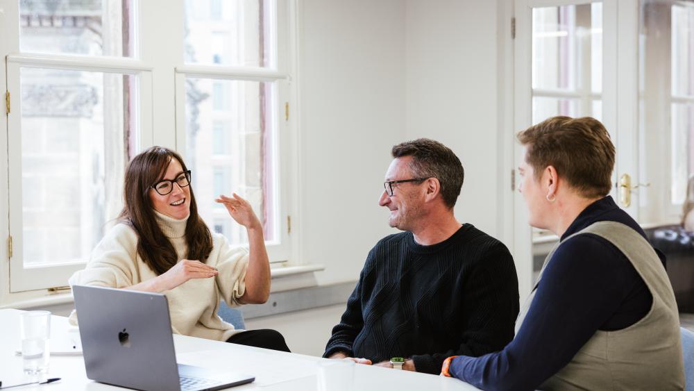 Three people sat at a table, one is explaining something