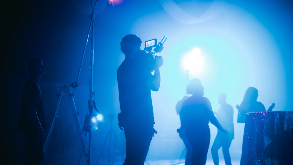 People filming in a dark TV studio, with a blue light slightly illuminating the scene.