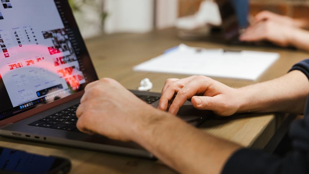 Hands typing on a laptop, their scren is visible and shows designs in progress