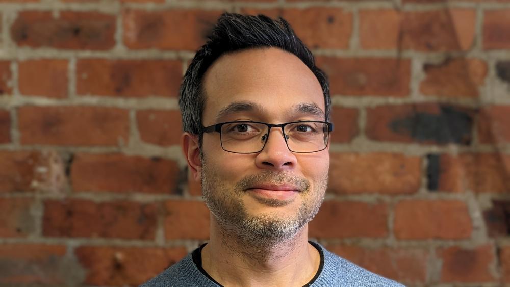 Jaron stood in front of a brick wall posing for a headshot