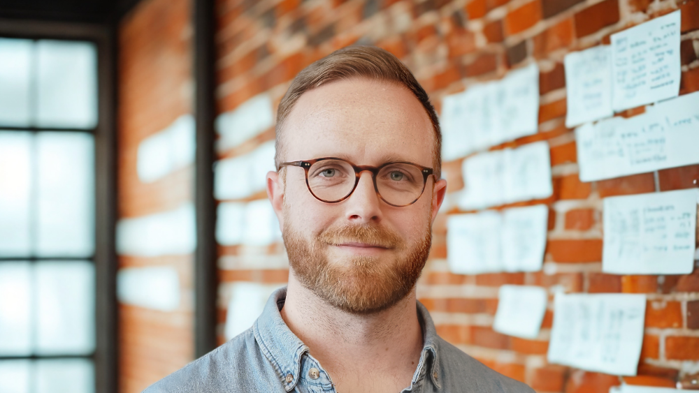 Paul posing for a headshot in front of a brick wall