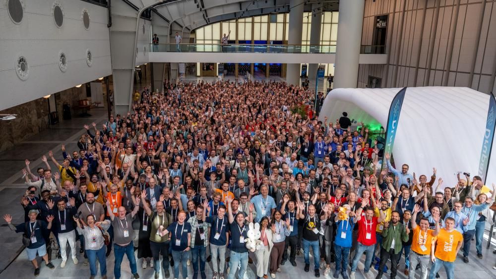 A large group photo of all of the developers at Drupal Con waving at the camera