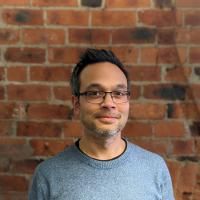 Jaron stood in front of a brick wall posing for a headshot